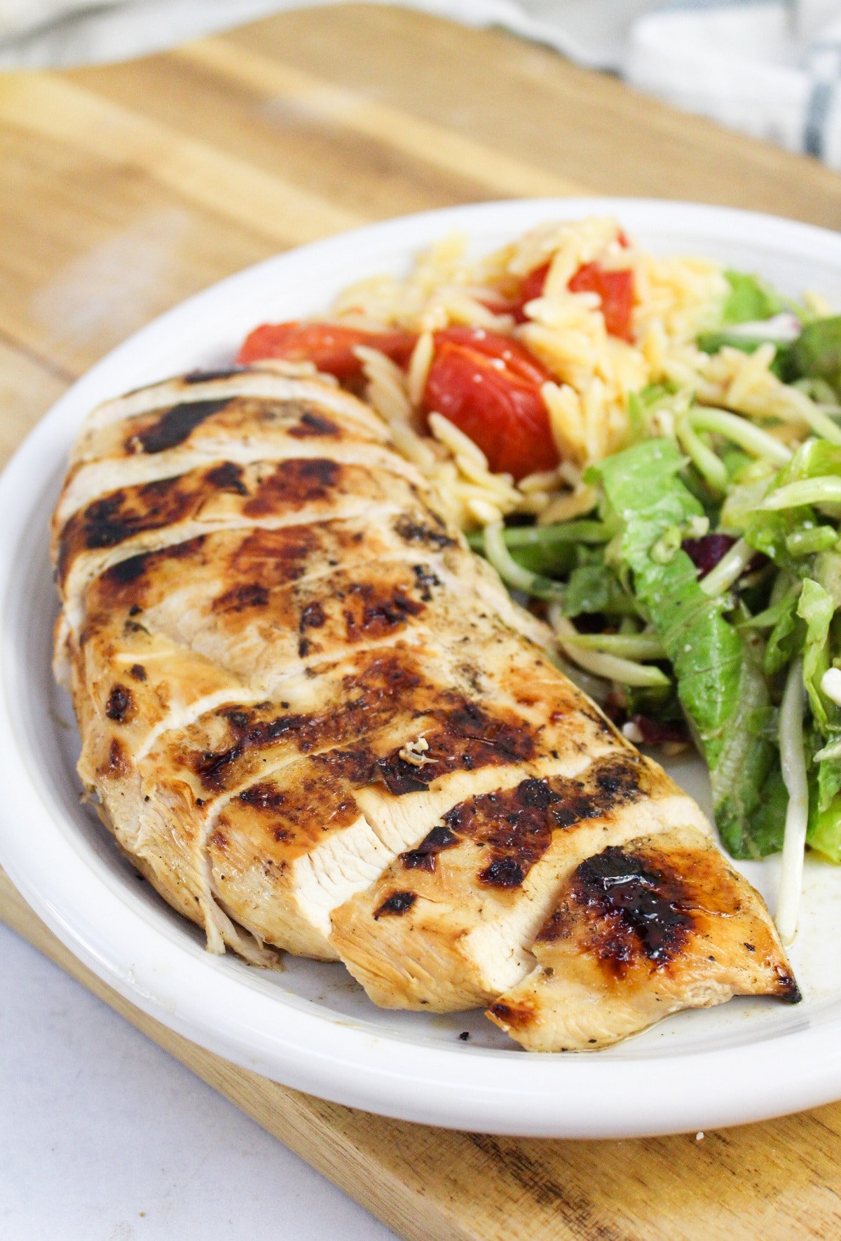 sliced grilled greek chicken on a plate with salad and rice.
