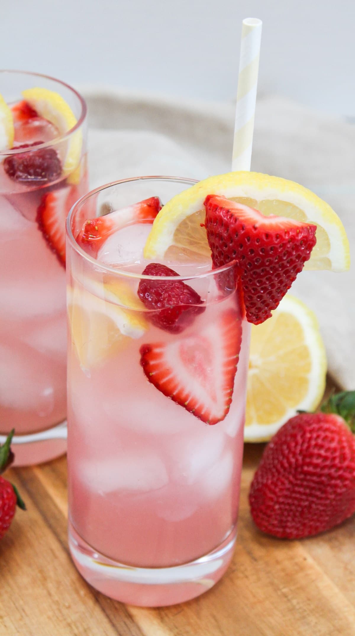 pink lemonade sangria in a tall glass garnished with strawberries, raspberries, and lemons.