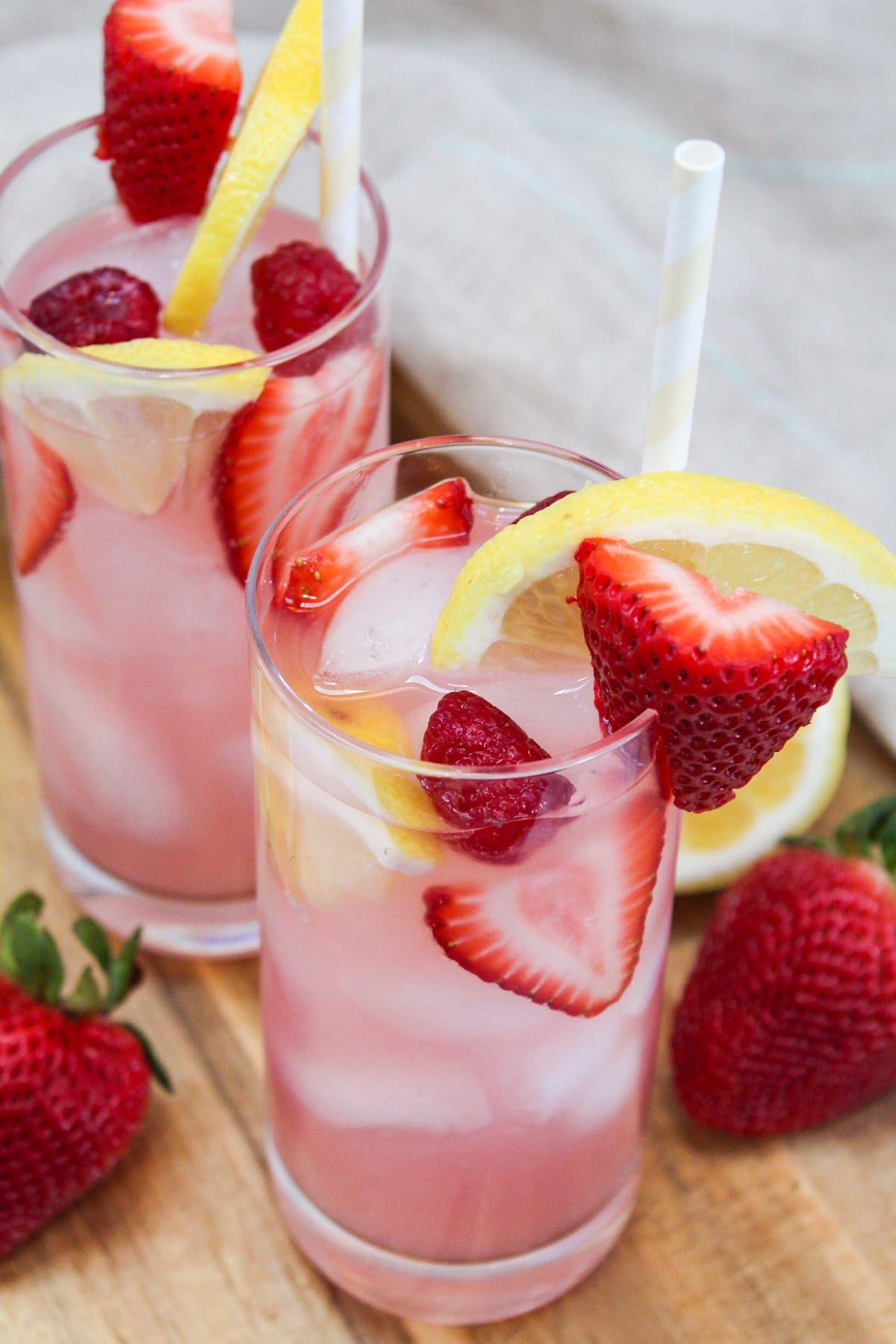 pink lemonade sangria in a tall glass garnished with strawberries, raspberries, and lemons.
