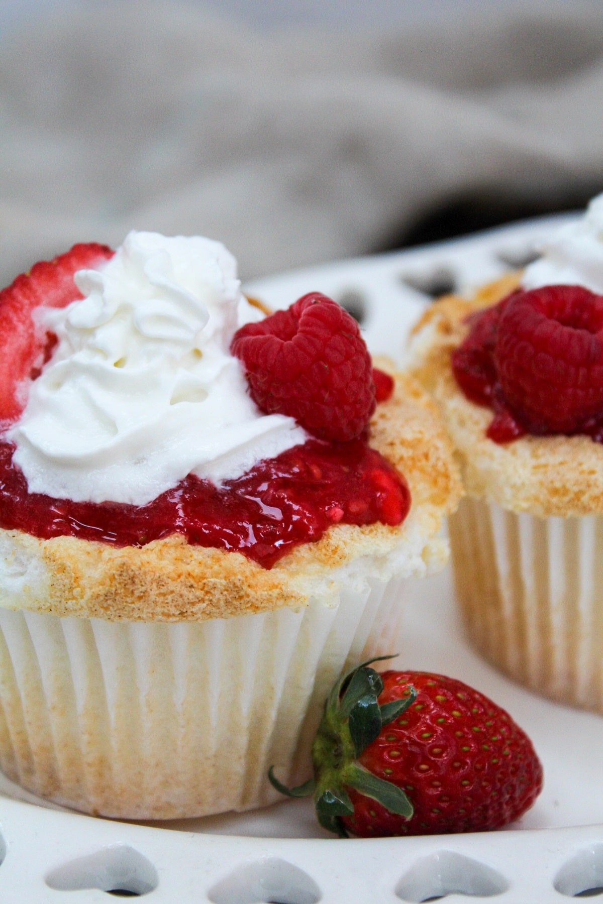 cupcake on a white plate with a strawberry on the side.