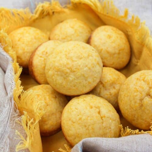 Muffins in a basket with a yellow cloth. Muffins are stacked on each other.