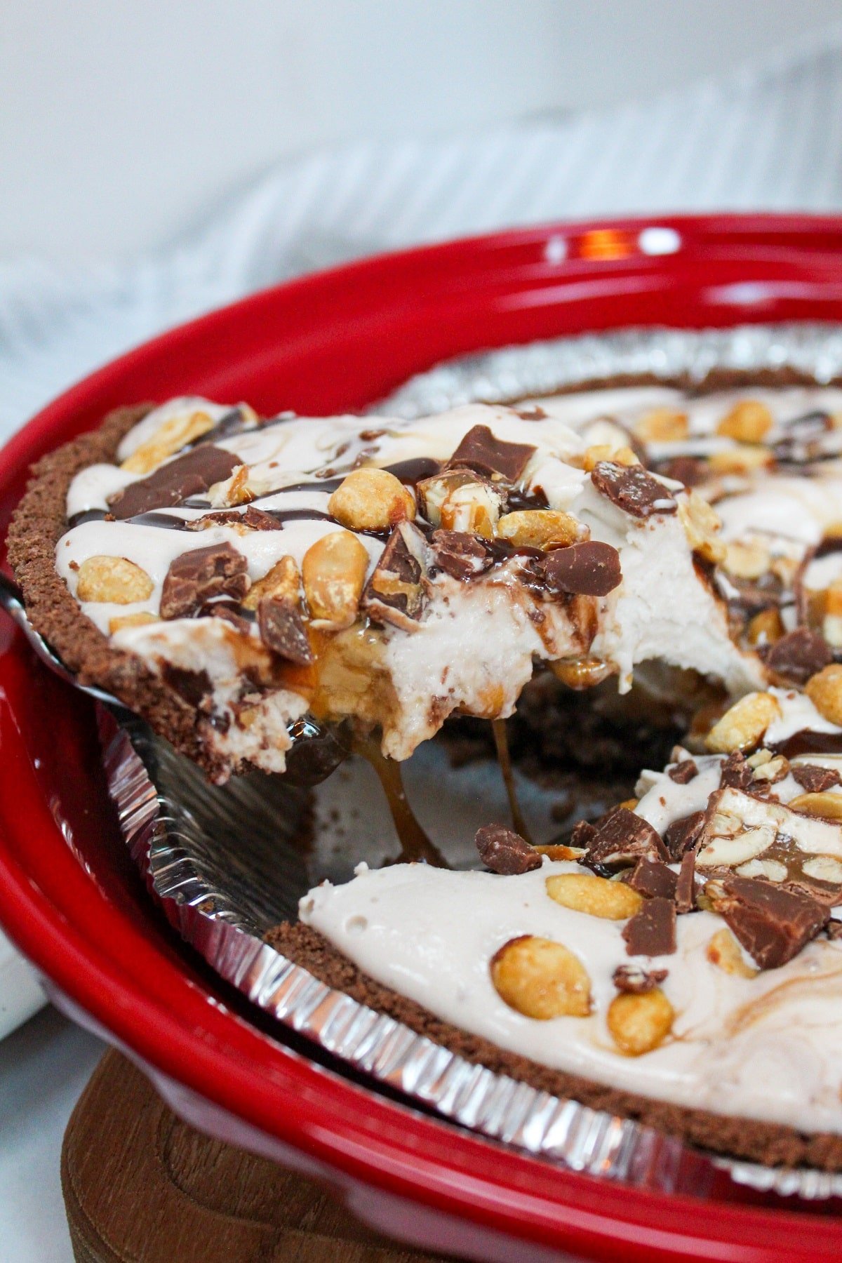 Snickers Ice Cream Cake in a red pie dish. The dessert is scooped from the cake to serve.