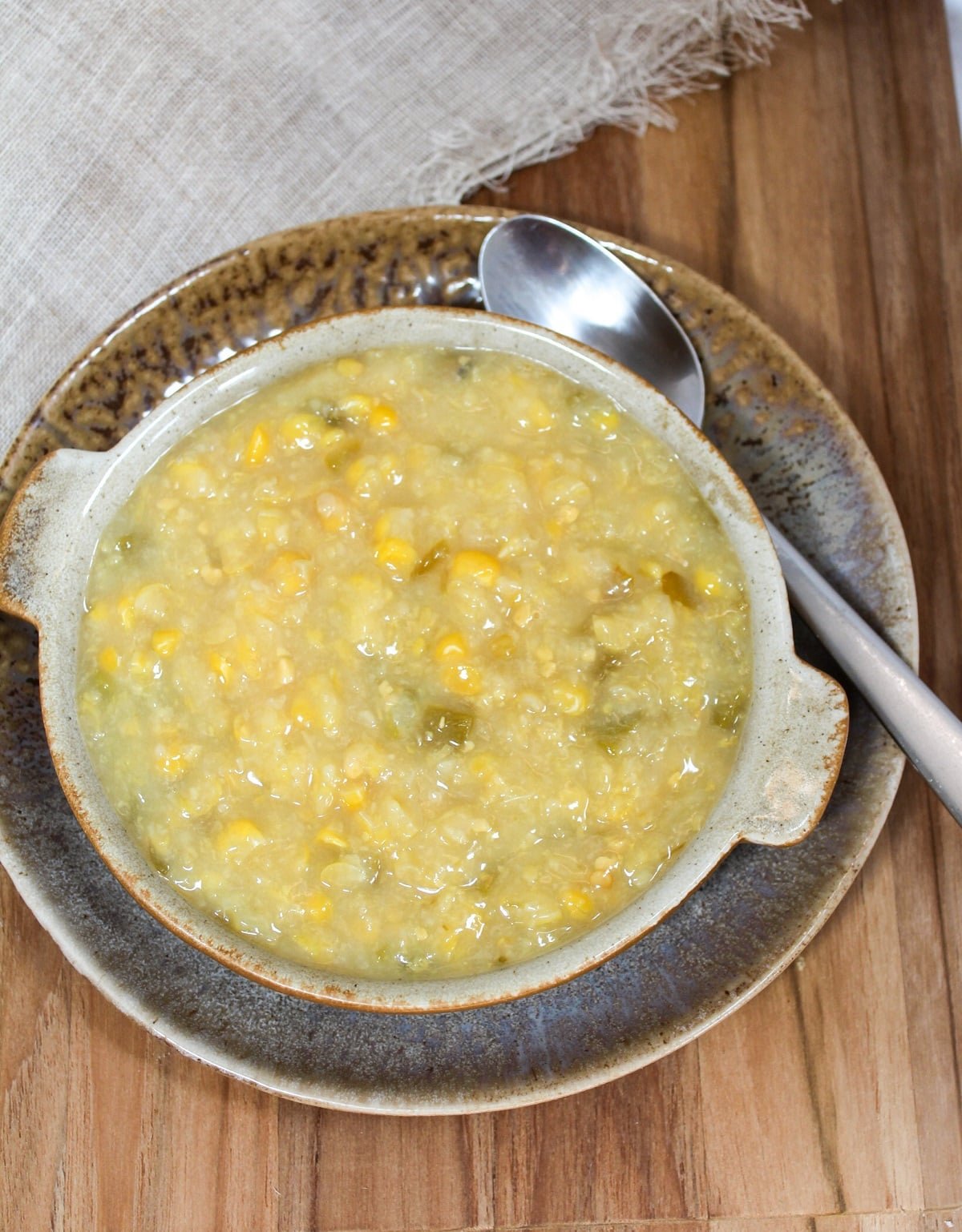 creamed corn with bits of chopped jalapenos in a brown bowl with a spoon on the side.