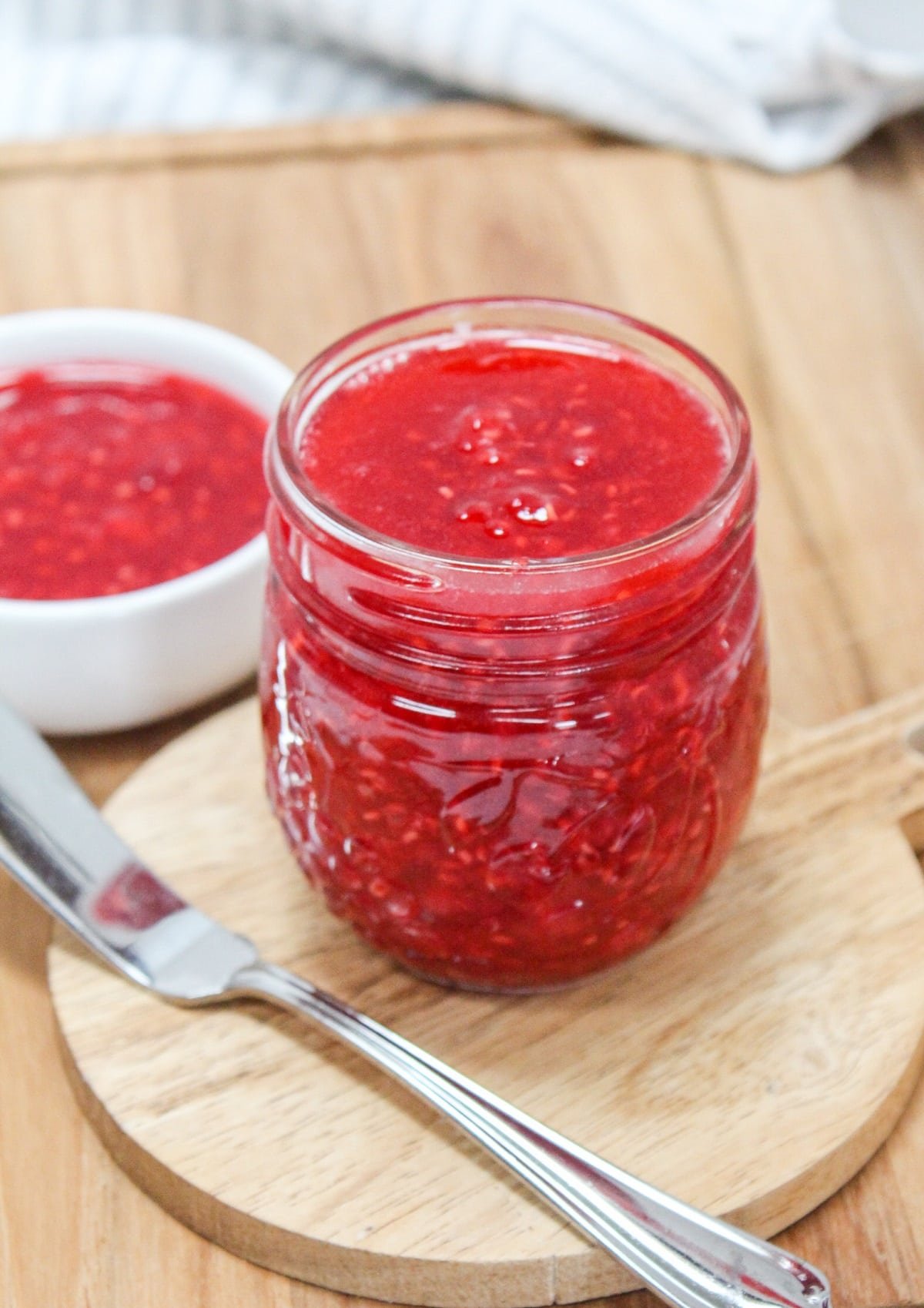 raspberry freezer jam in a glass jar with a knife on the side.