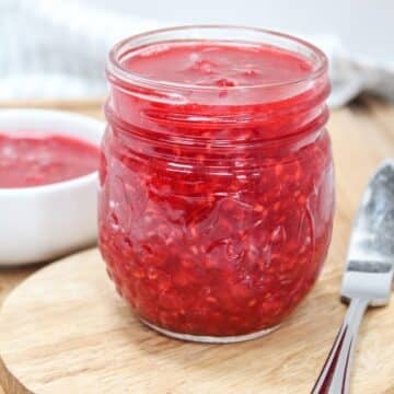 raspberry freezer jam in a glass jar with a knife on the side.