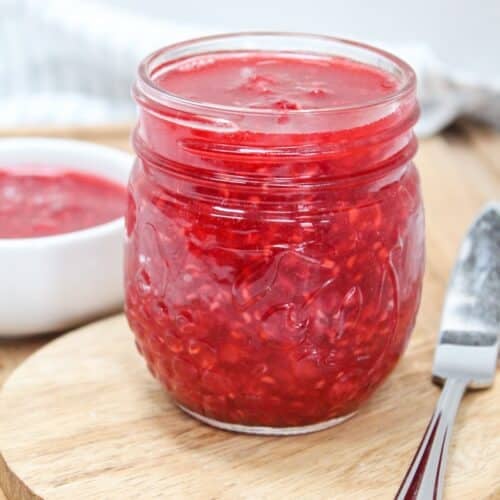 raspberry freezer jam in a glass jar with a knife on the side.